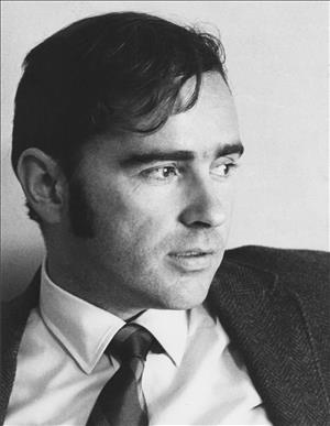 Head and shoulders portrait of a young man in a tie with dark hair and sideburns. 